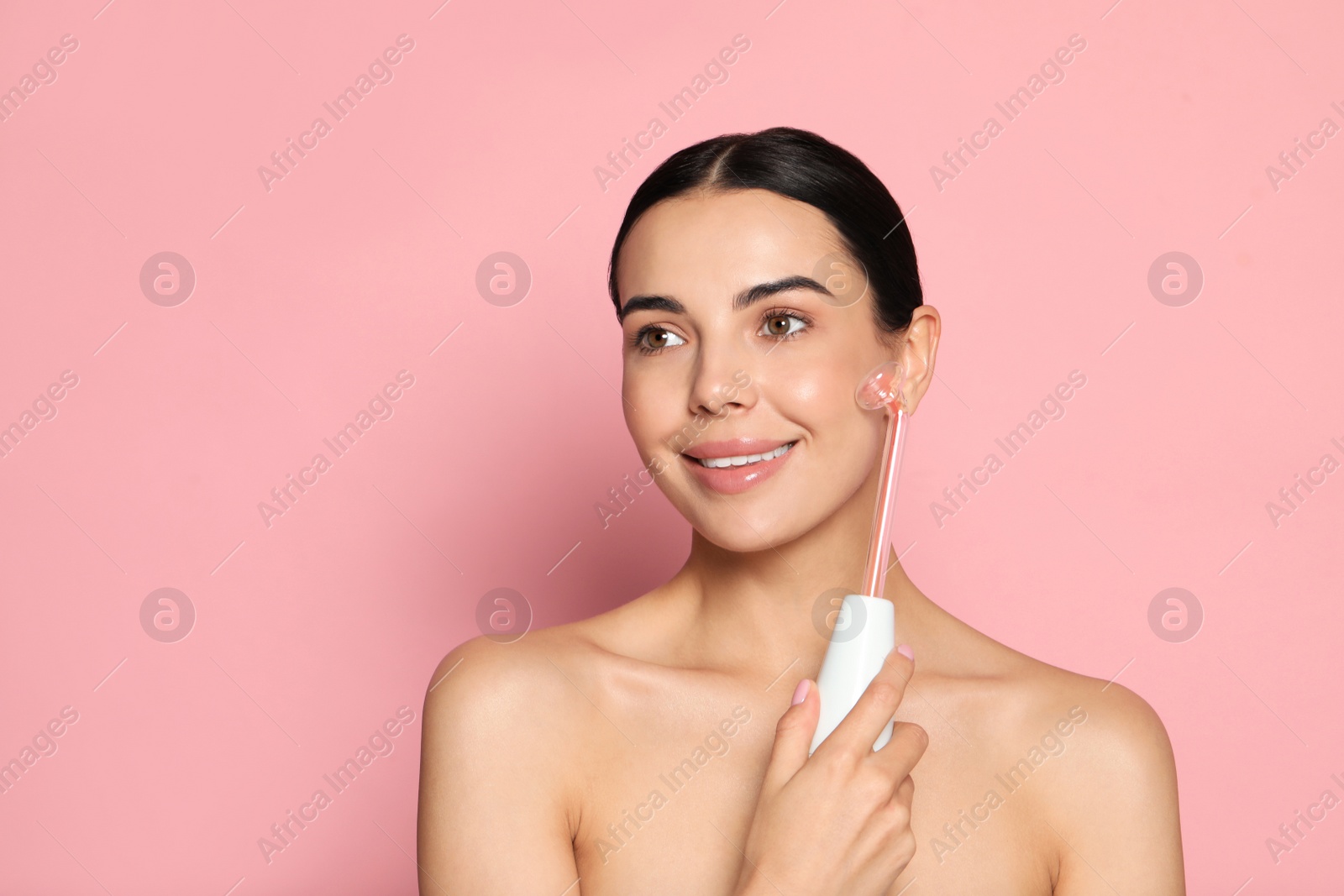 Photo of Woman using high frequency darsonval device on pink background. Space for text