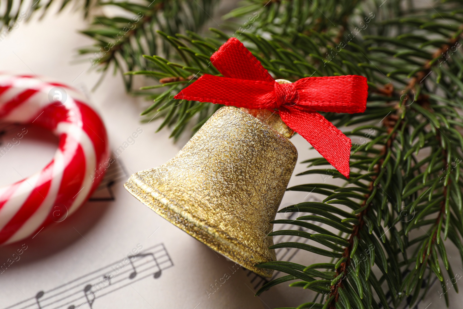 Photo of Golden shiny bell with red bow and fir branches on music sheet, closeup. Christmas decoration