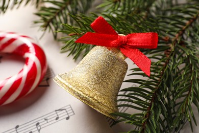 Photo of Golden shiny bell with red bow and fir branches on music sheet, closeup. Christmas decoration