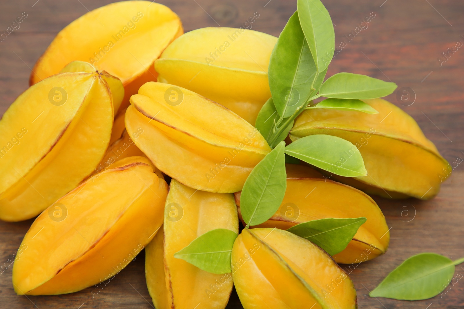 Photo of Many delicious ripe carambolas with leaves on wooden table, closeup