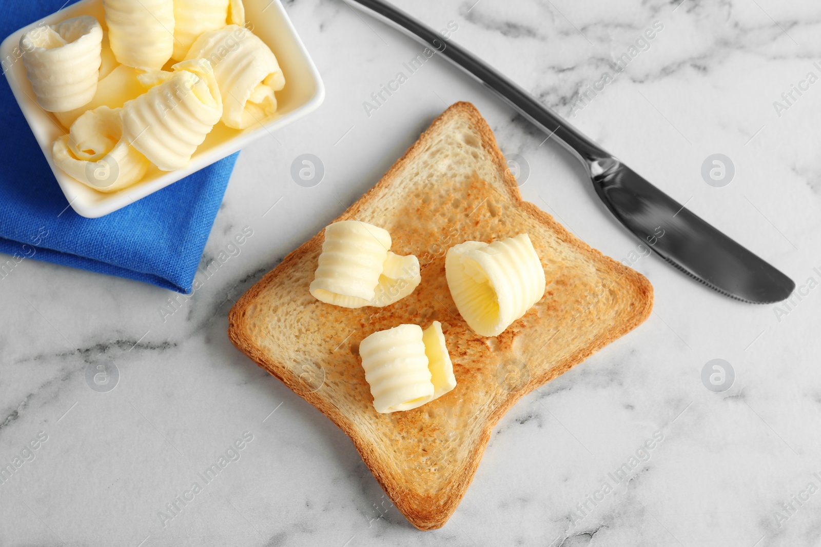 Photo of Toasted bread with butter curls on table, top view