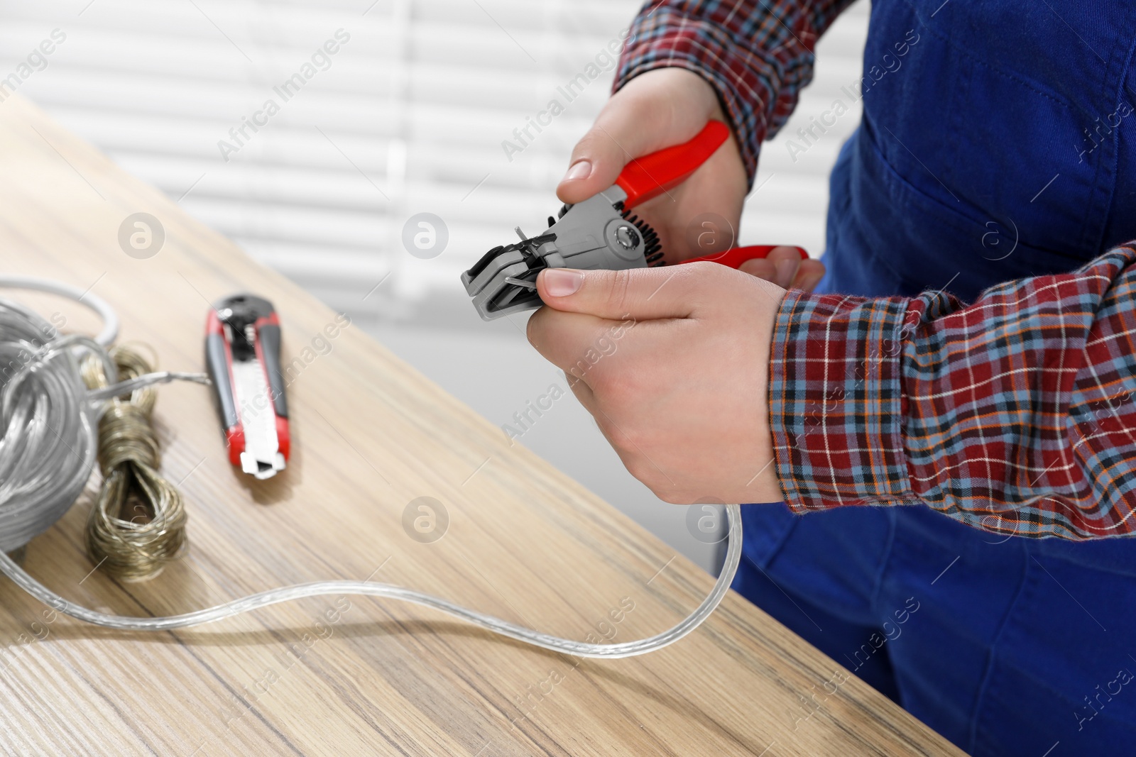 Photo of Professional electrician stripping wiring at wooden table, closeup view