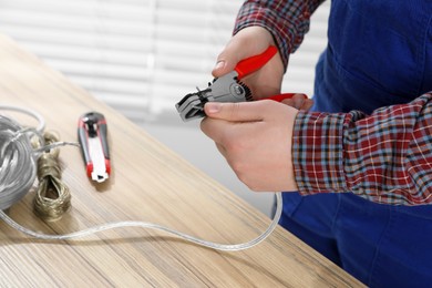 Photo of Professional electrician stripping wiring at wooden table, closeup view
