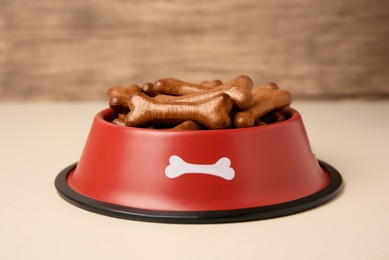 Photo of Red bowl with bone shaped dog cookies on light table, closeup