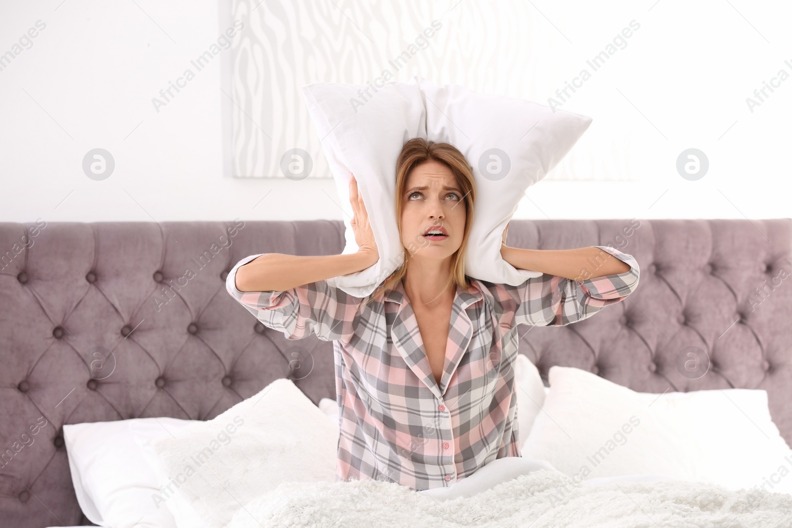 Photo of Young woman covering ears with pillow in bed at home. Sleeping disorder