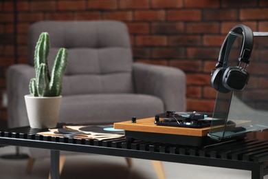 Photo of Stylish turntable with vinyl records, headphones and houseplant on table indoors