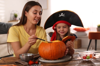 Photo of Mother and daughter making pumpkin jack o'lantern at table indoors. Halloween celebration