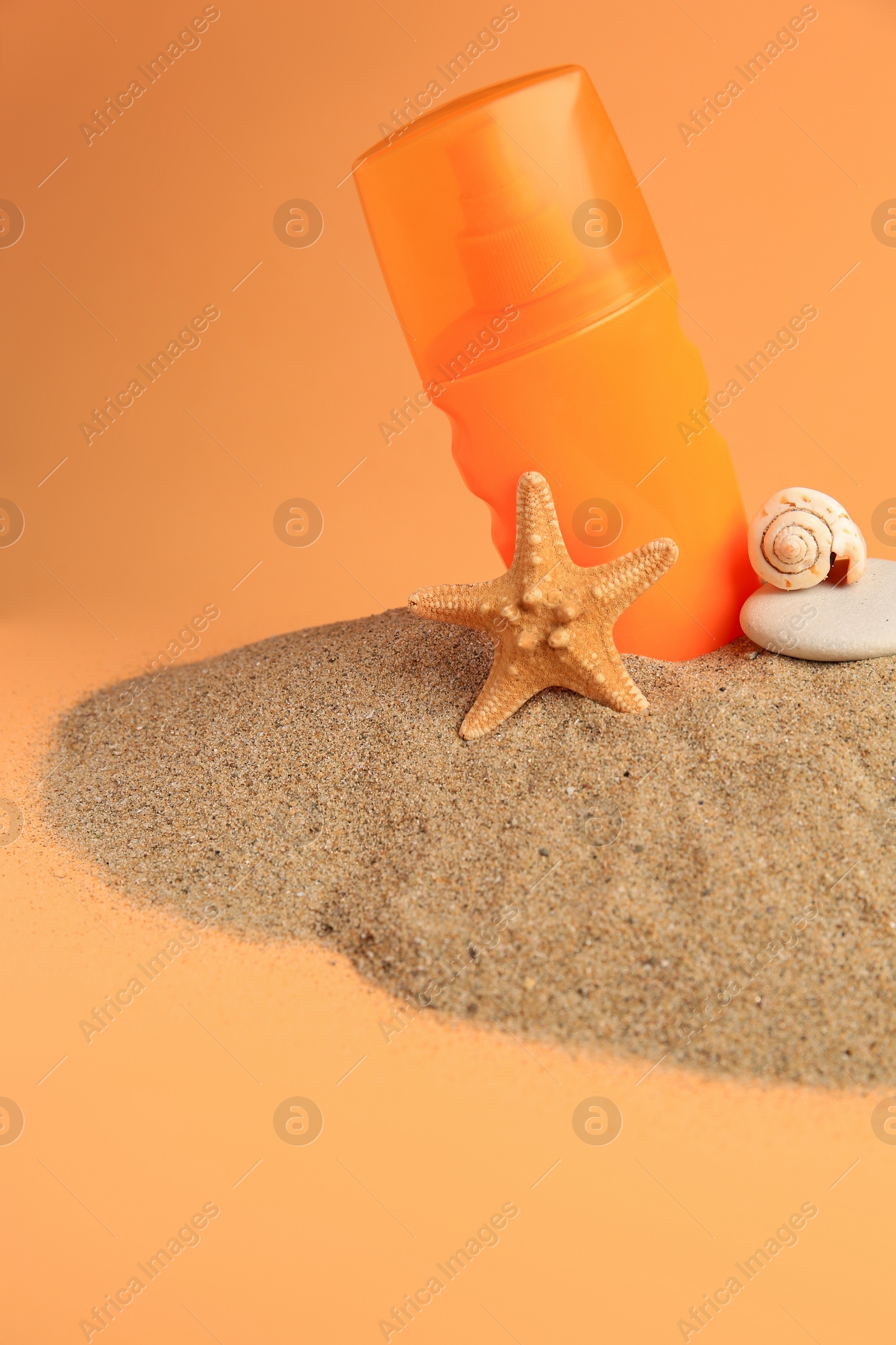 Photo of Sand with bottle of sunscreen, starfish, stone and seashell against orange background. Sun protection