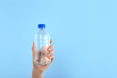 Photo of Woman holding plastic bottle with water on color background. Space for text