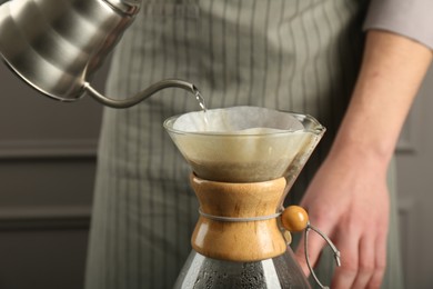 Photo of Man pouring hot water into glass chemex coffeemaker with paper filter and coffee on grey background, closeup