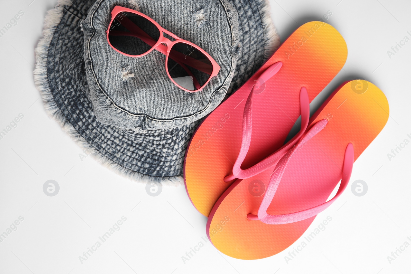 Photo of Sunglasses, hat and bright flip flops on white background, flat lay. Beach accessories