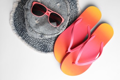 Sunglasses, hat and bright flip flops on white background, flat lay. Beach accessories