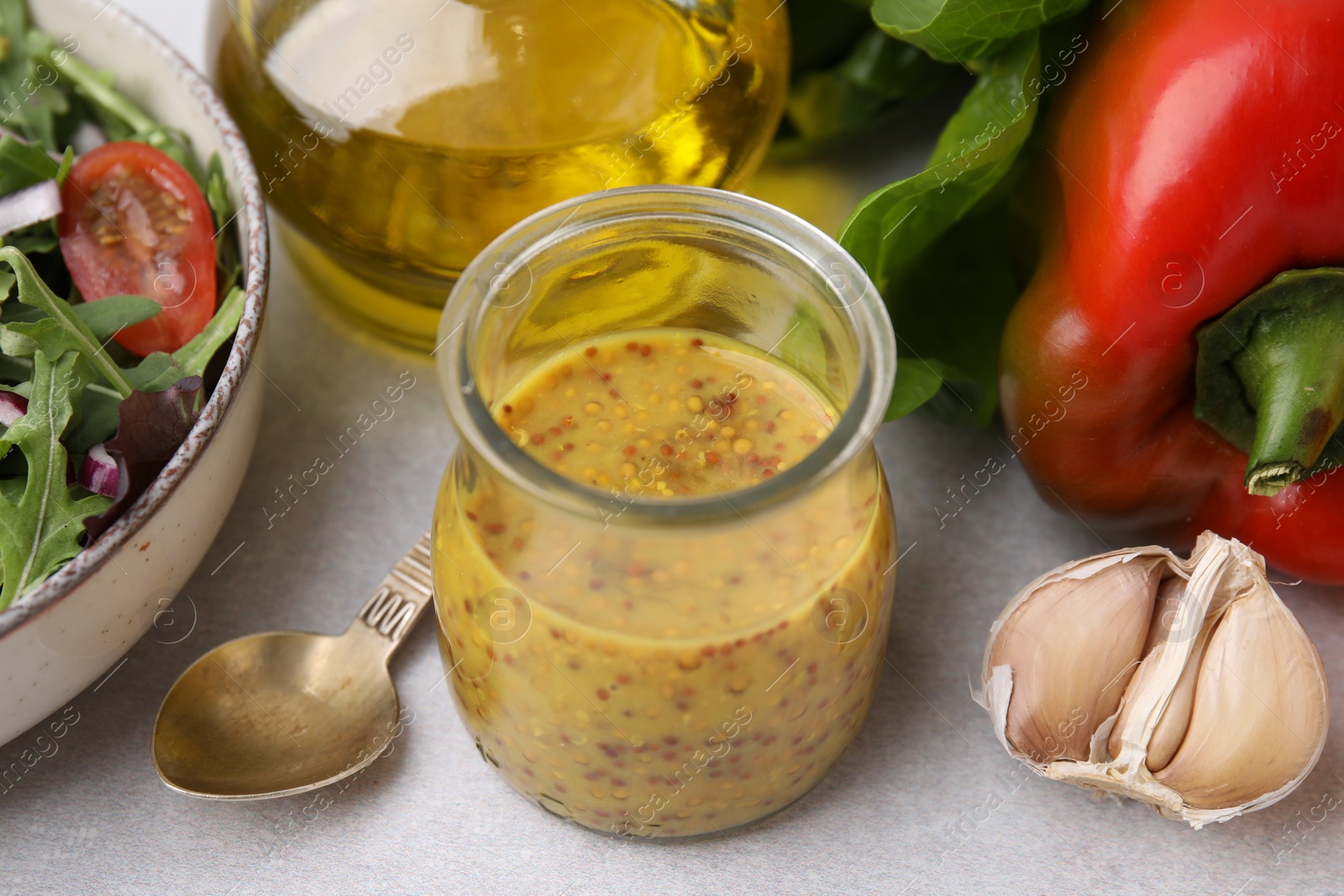 Photo of Tasty vinegar based sauce (Vinaigrette) in jar, salad and products on light table, closeup