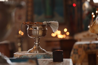 Photo of Silver vessel with holy water and brush on stand in church. Baptism ceremony