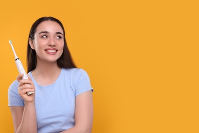 Happy young woman holding electric toothbrush on yellow background, space for text