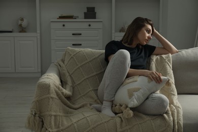 Sad young woman sitting on sofa at home, space for text