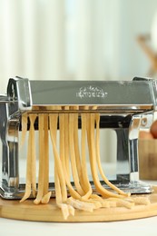 Photo of Pasta maker with raw dough on white table, closeup