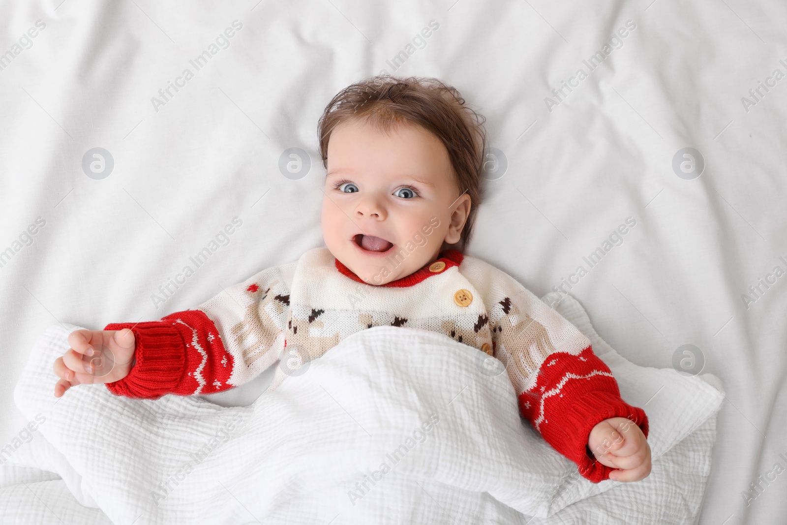 Photo of Cute little baby in Christmas sweater on soft bed, top view