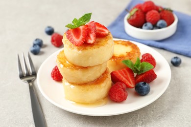 Photo of Delicious cottage cheese pancakes with fresh berries, mint and honey on light grey table