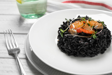 Delicious black risotto with seafood on white wooden table, closeup