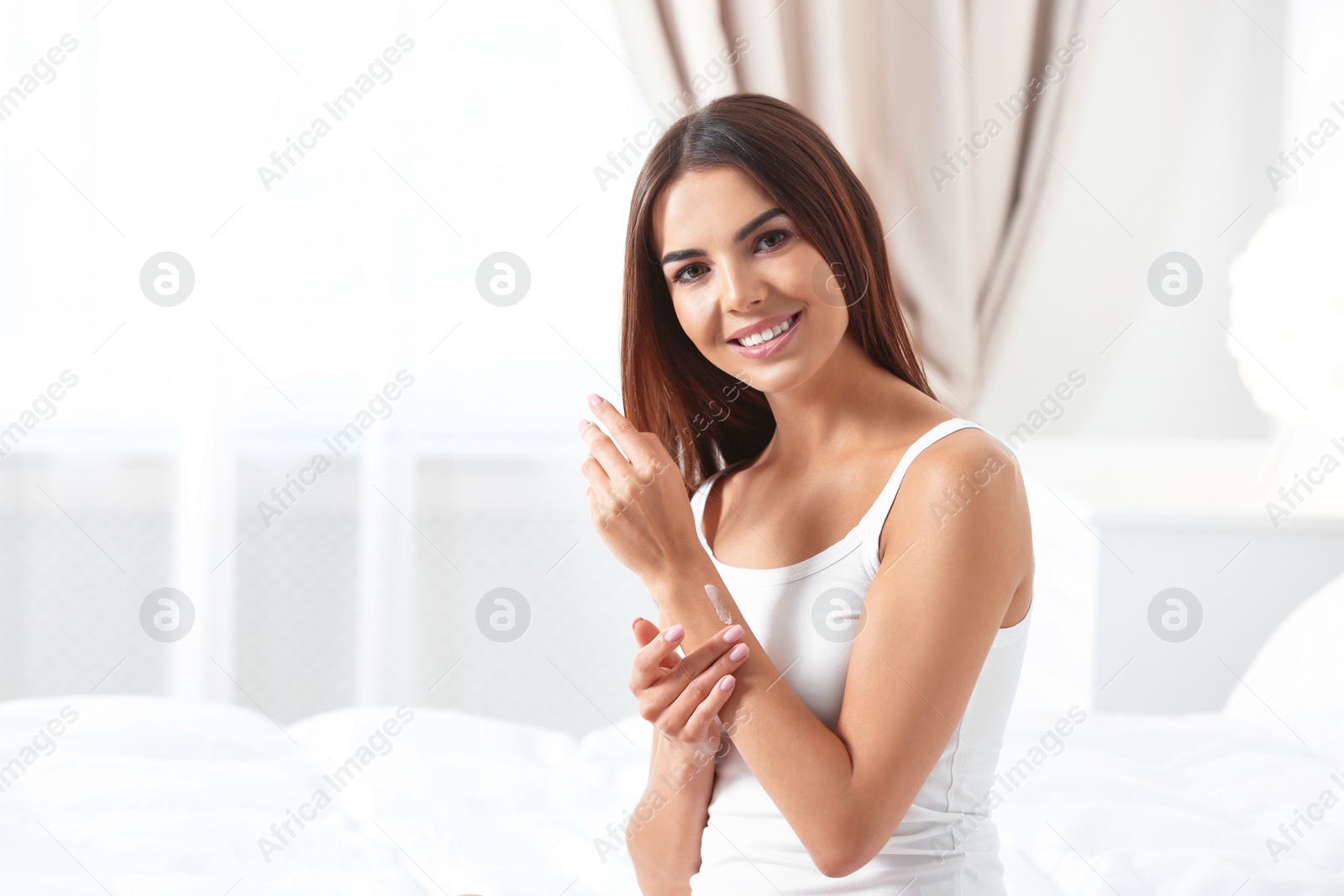 Photo of Young woman applying cream indoors, space for text. Beauty and body care