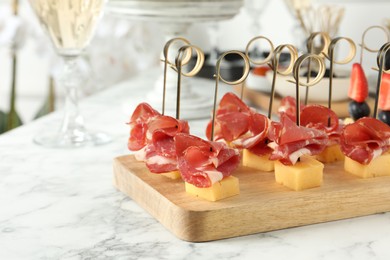 Photo of Tasty canapes with cheese and ham on white marble table, closeup. Space for text