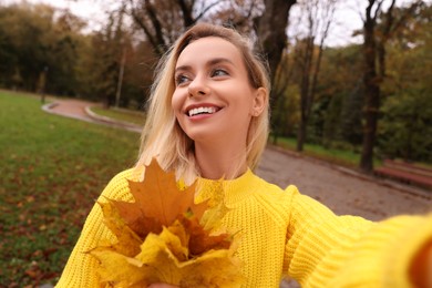 Portrait of happy woman with autumn leaves taking selfie in park