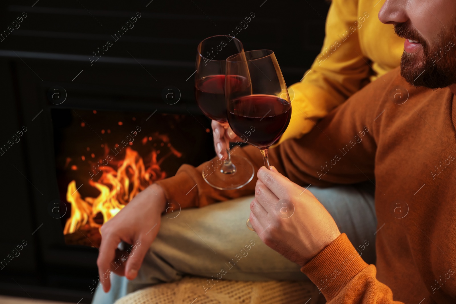 Photo of Lovely couple with glasses of wine spending time together near fireplace at home, closeup