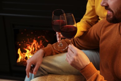 Lovely couple with glasses of wine spending time together near fireplace at home, closeup