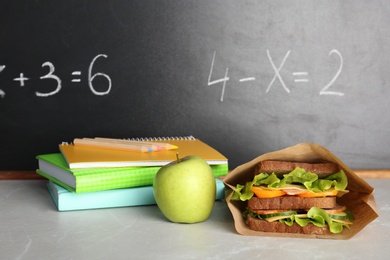 Photo of Healthy food for school child and stationery on table near blackboard with chalk written sums