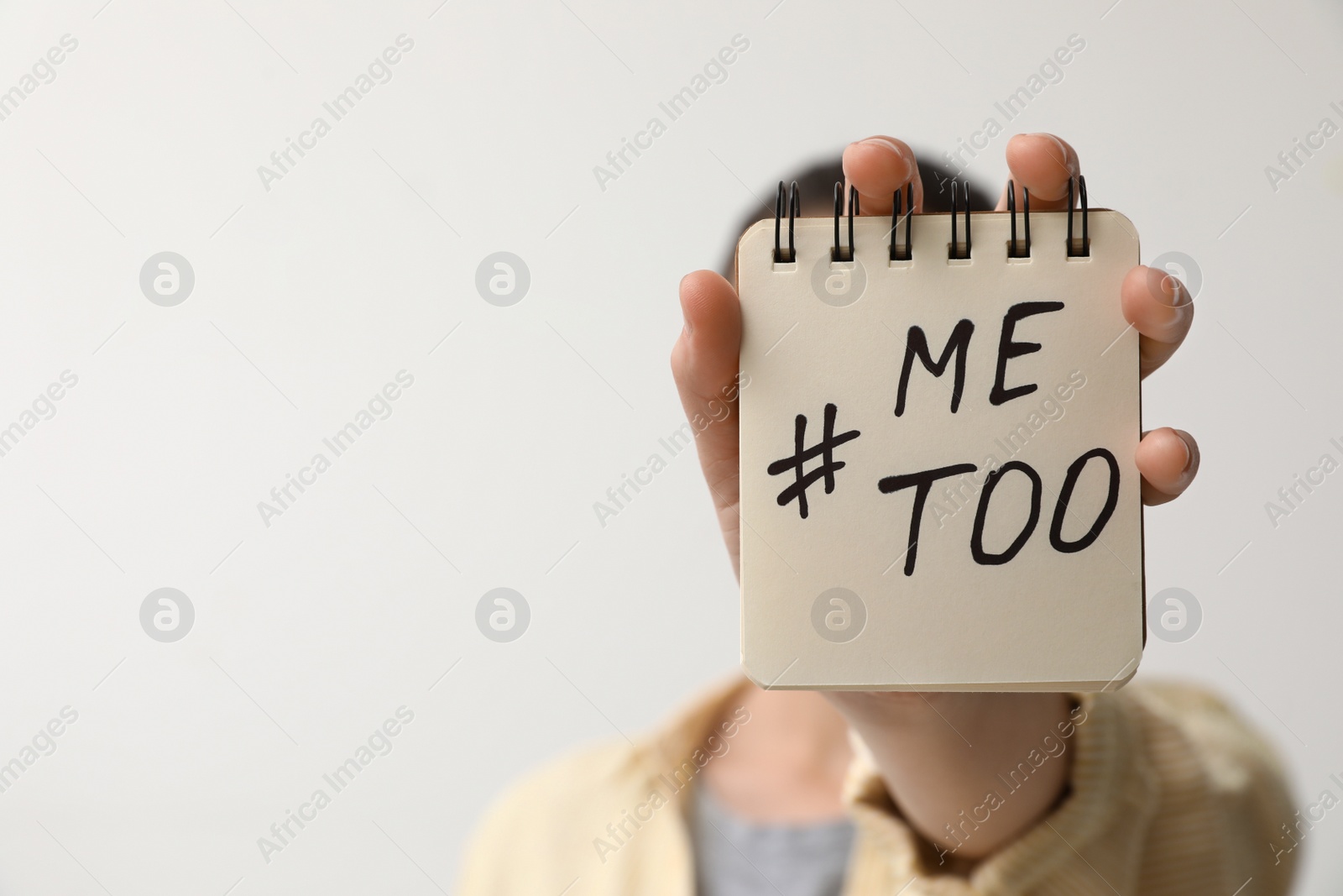 Photo of Woman holding notebook with hashtag MeToo against light background, closeup. Stop sexual assault