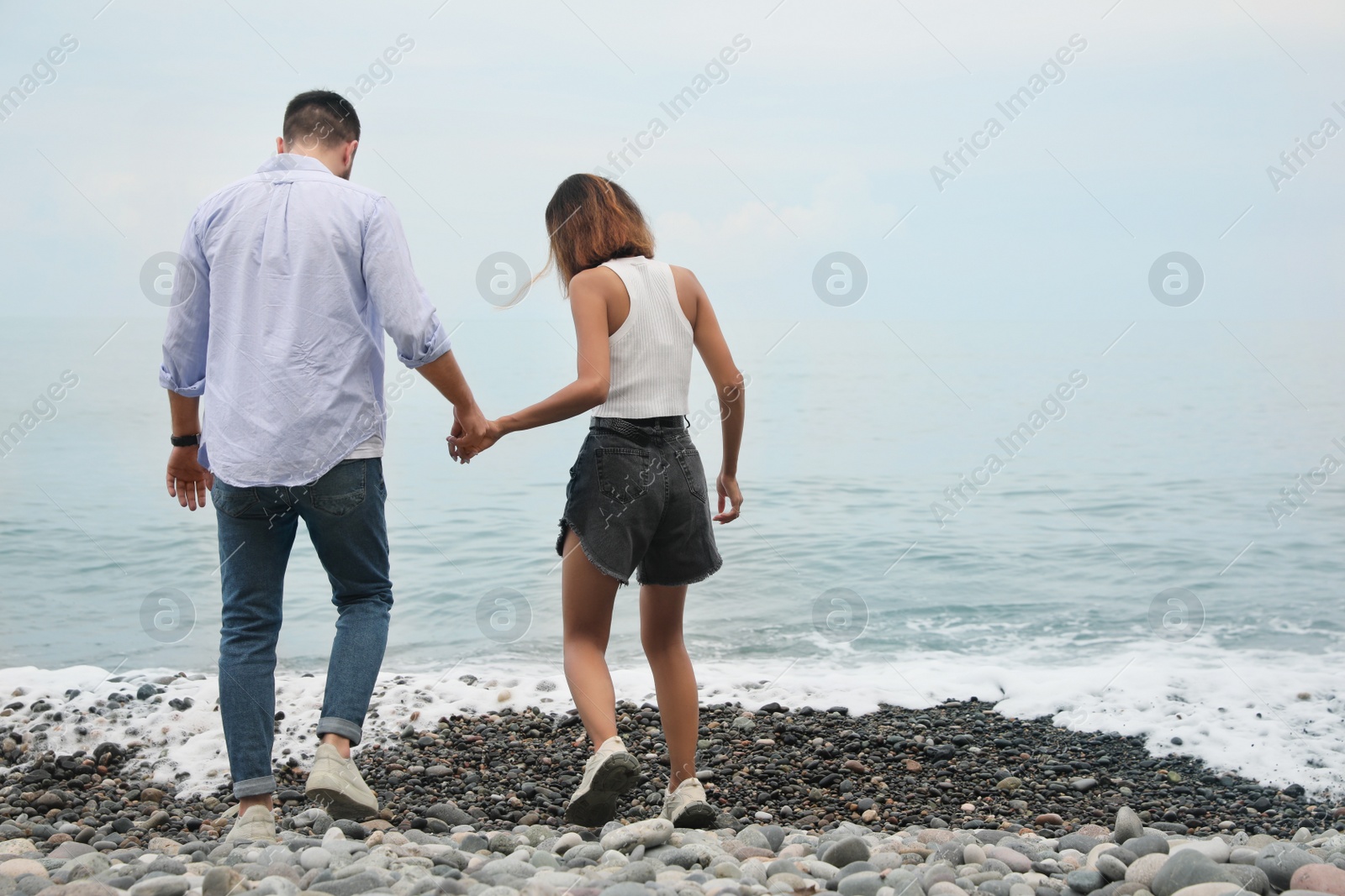 Photo of Young couple walking on beach near sea, back view. Space for text