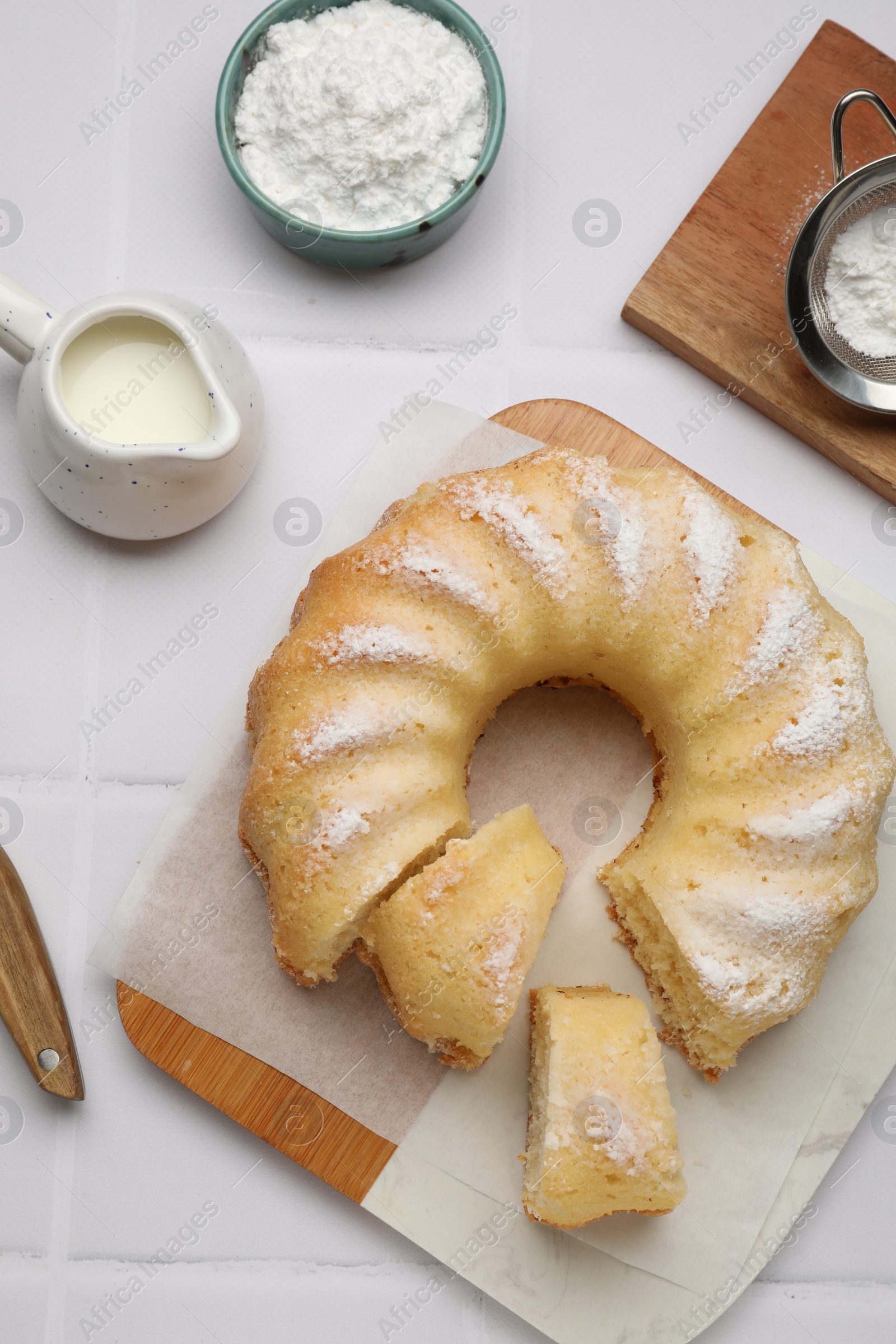 Photo of Delicious sponge cake served on white tiled table, flat lay