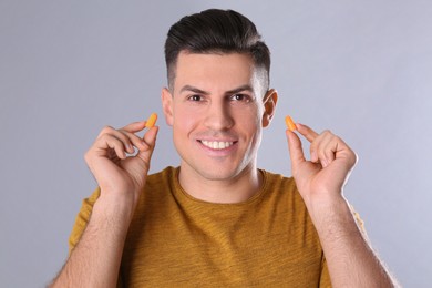 Photo of Man inserting foam ear plugs on grey background