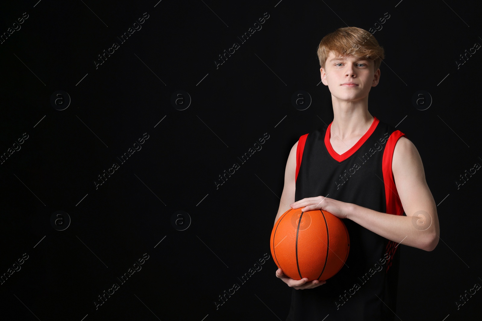 Photo of Teenage boy with basketball ball on black background. Space for text