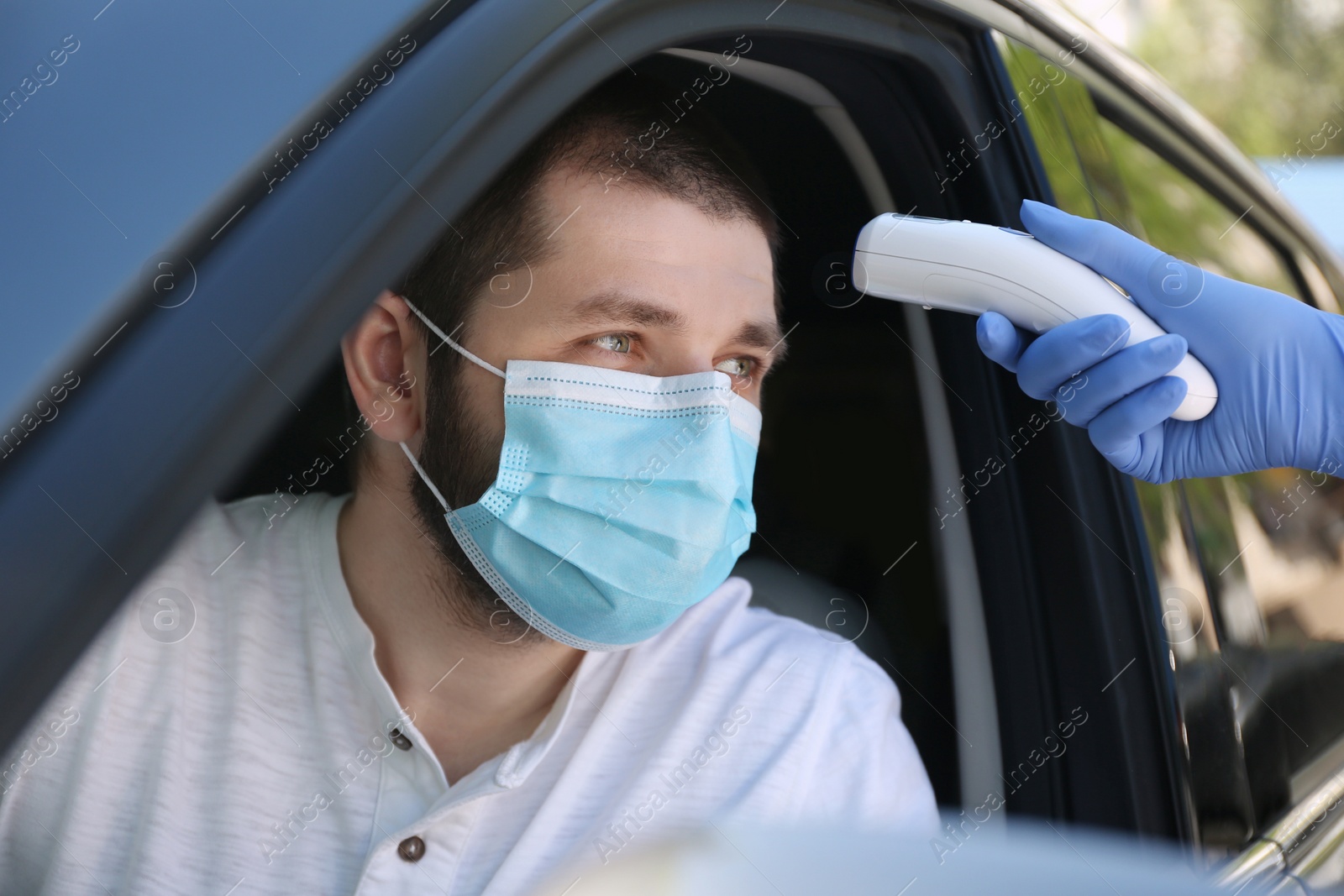 Photo of Doctor measuring driver's temperature with non contact infrared thermometer outdoors