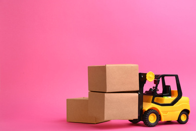 Photo of Forklift model and carton boxes on pink background, space for text. Courier service