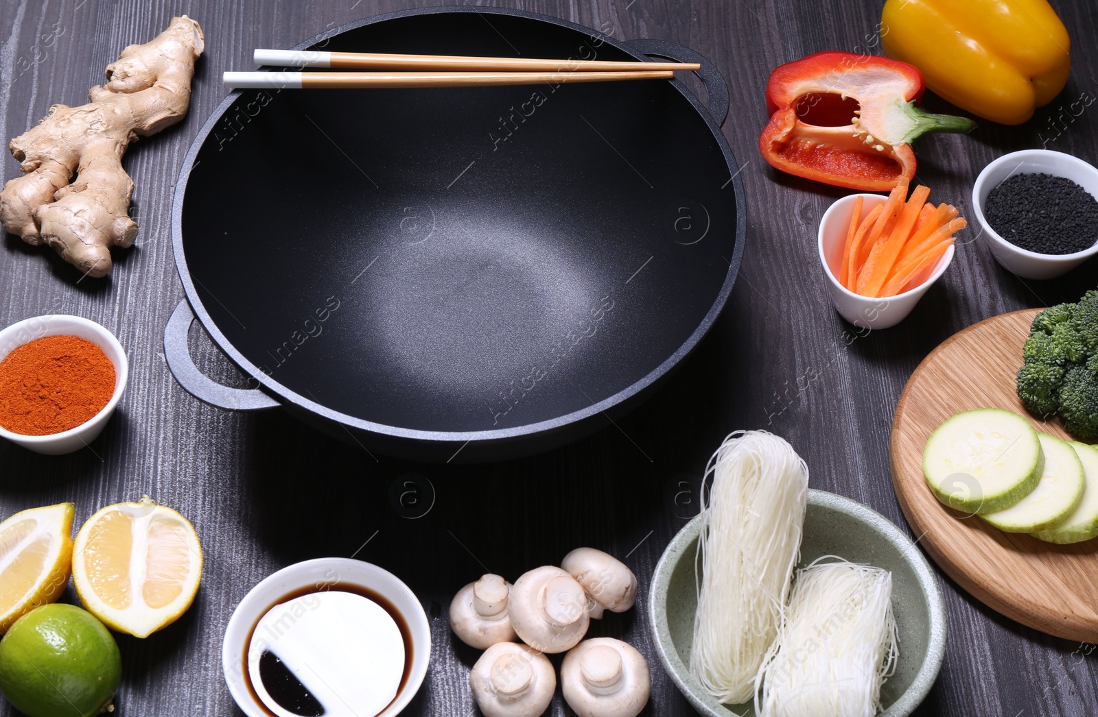 Photo of Empty iron wok, chopsticks and ingredients on dark grey wooden table