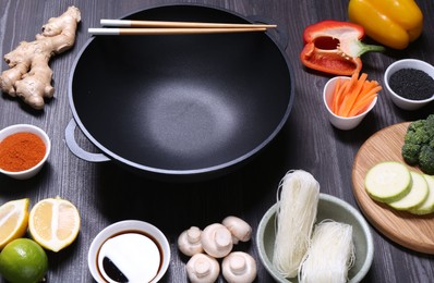 Photo of Empty iron wok, chopsticks and ingredients on dark grey wooden table