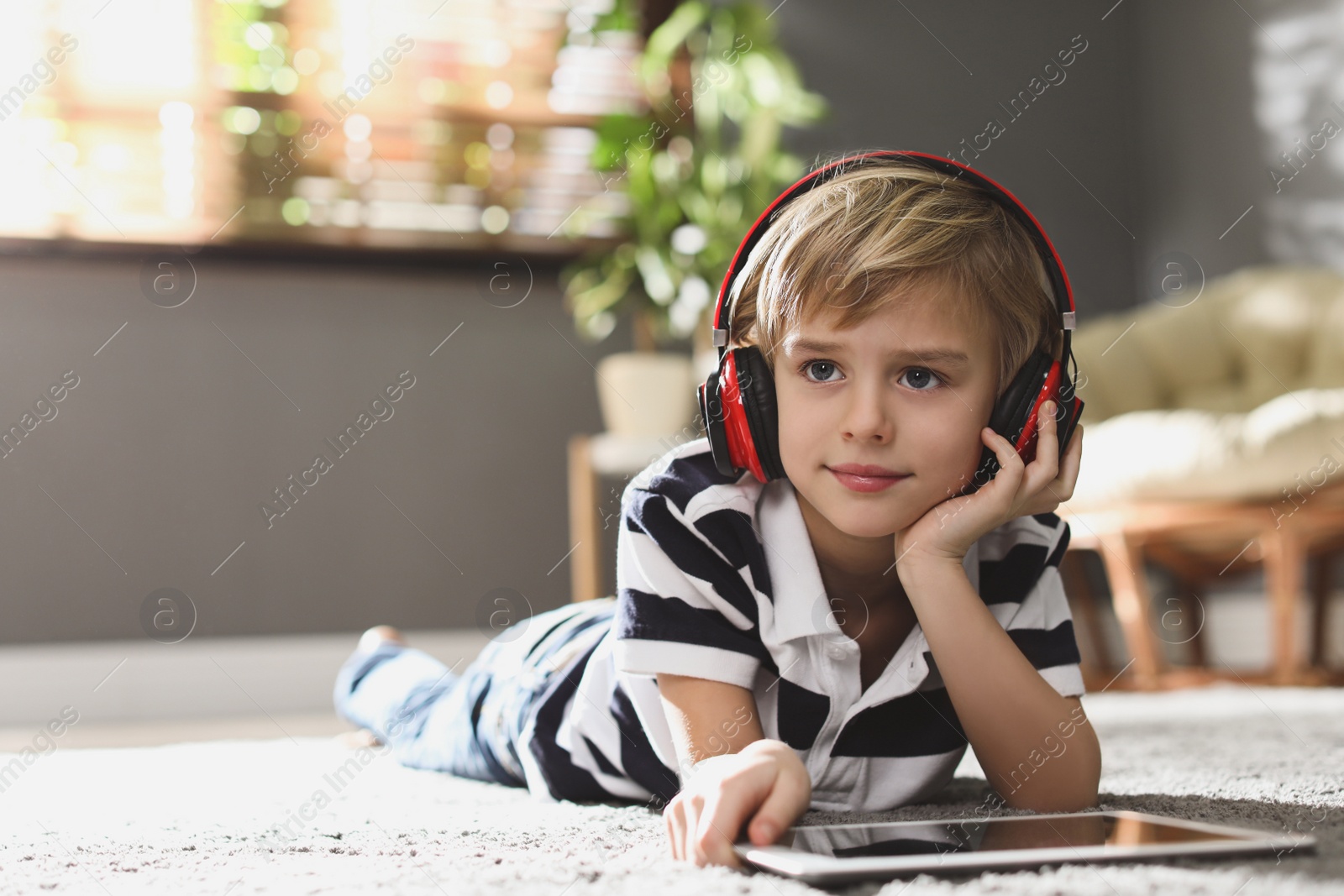 Photo of Cute little boy with headphones and tablet listening to audiobook at home