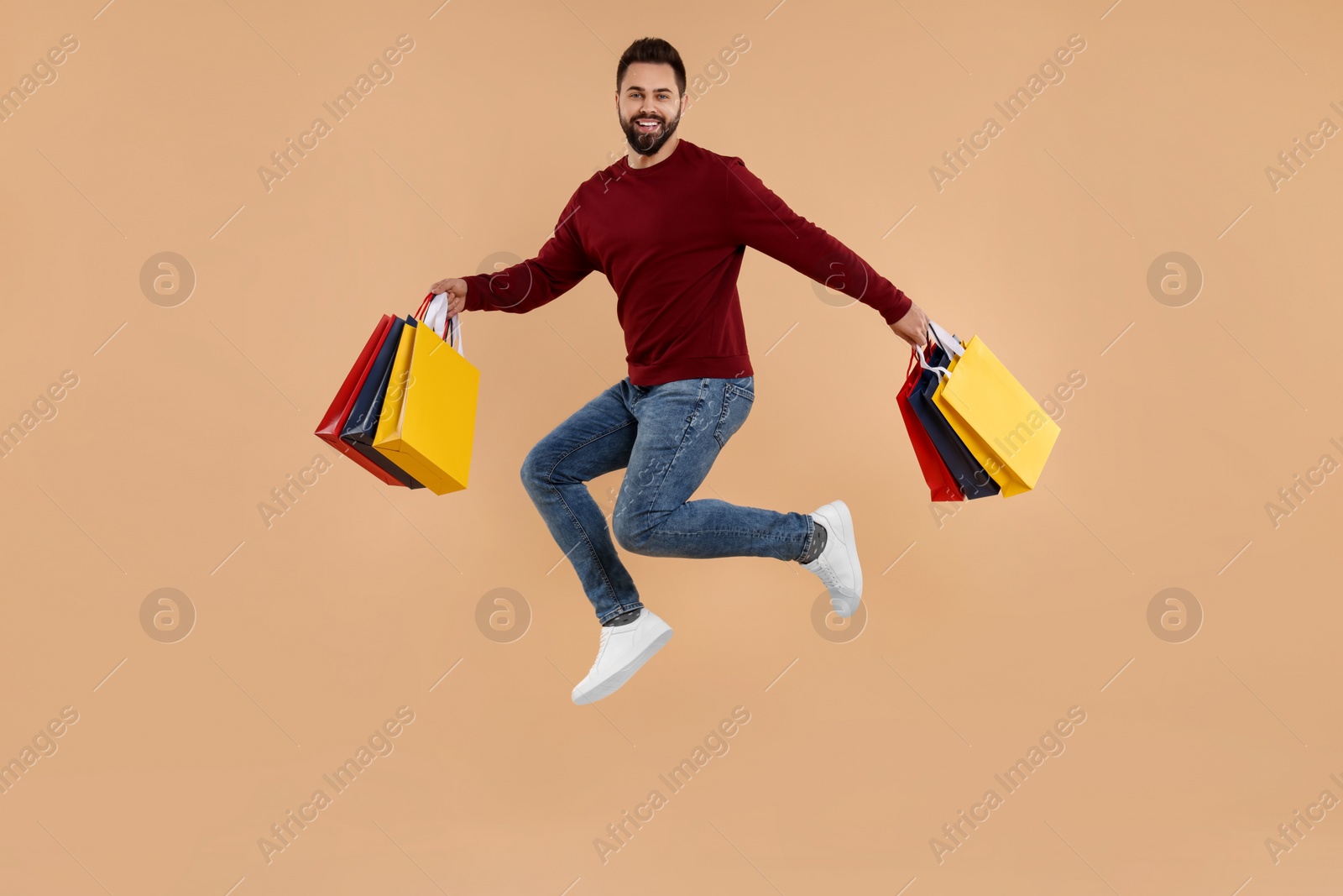 Photo of Happy man with many paper shopping bags jumping on beige background