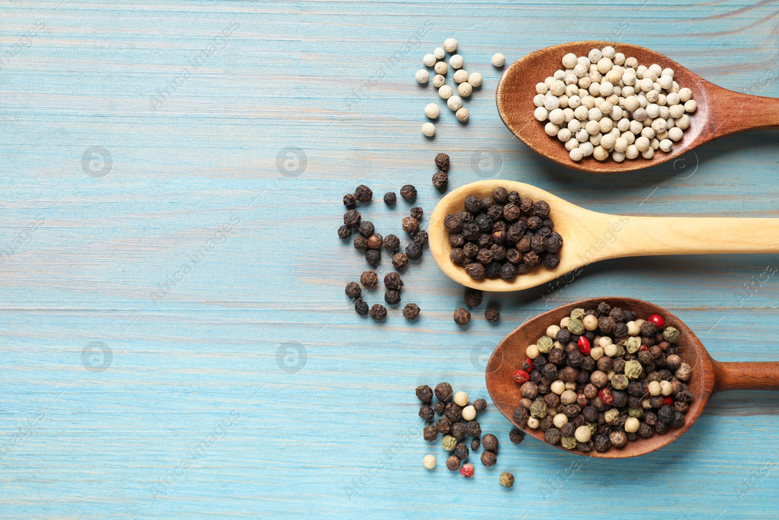 Photo of Aromatic spice. Different peppers in spoons on light blue wooden table, flat lay. Space for text