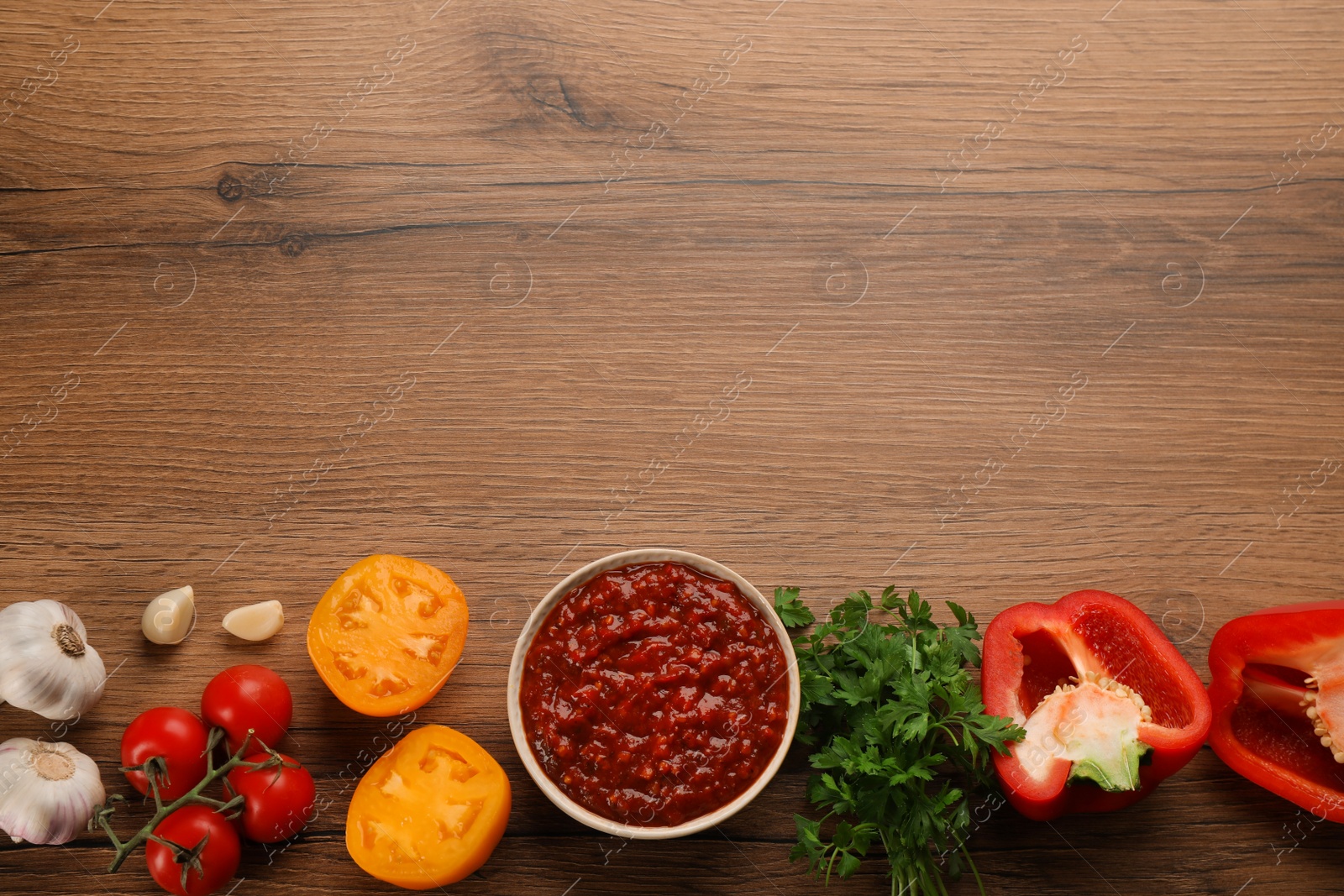 Photo of Delicious adjika sauce in bowl and ingredients on wooden table, flat lay. Space for text