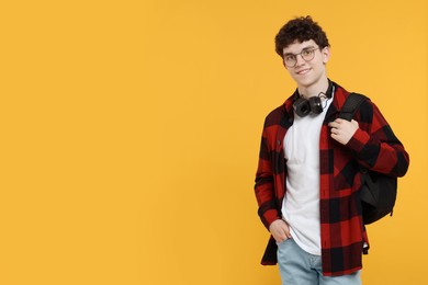Photo of Portrait of student with backpack, headphones and glasses on orange background. Space for text