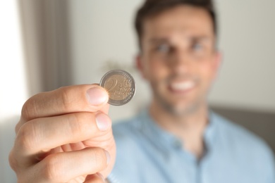 Photo of Young man holding coin at home, focus on hand