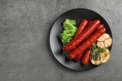 Photo of Delicious grilled sausages and vegetables on grey table, top view. Space for text