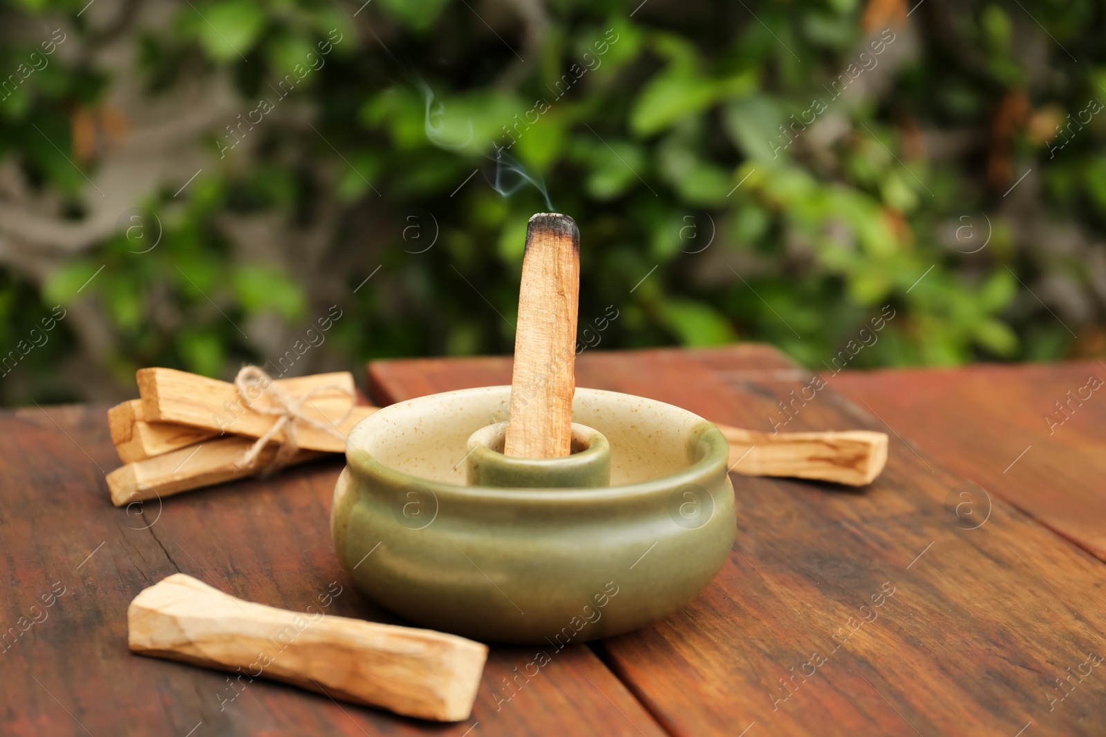 Photo of Palo Santo stick smoldering in holder on wooden table outdoors