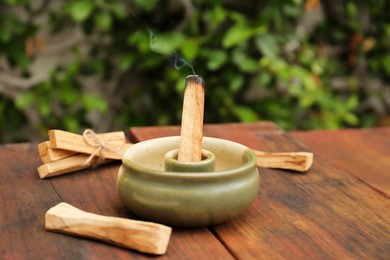 Palo Santo stick smoldering in holder on wooden table outdoors