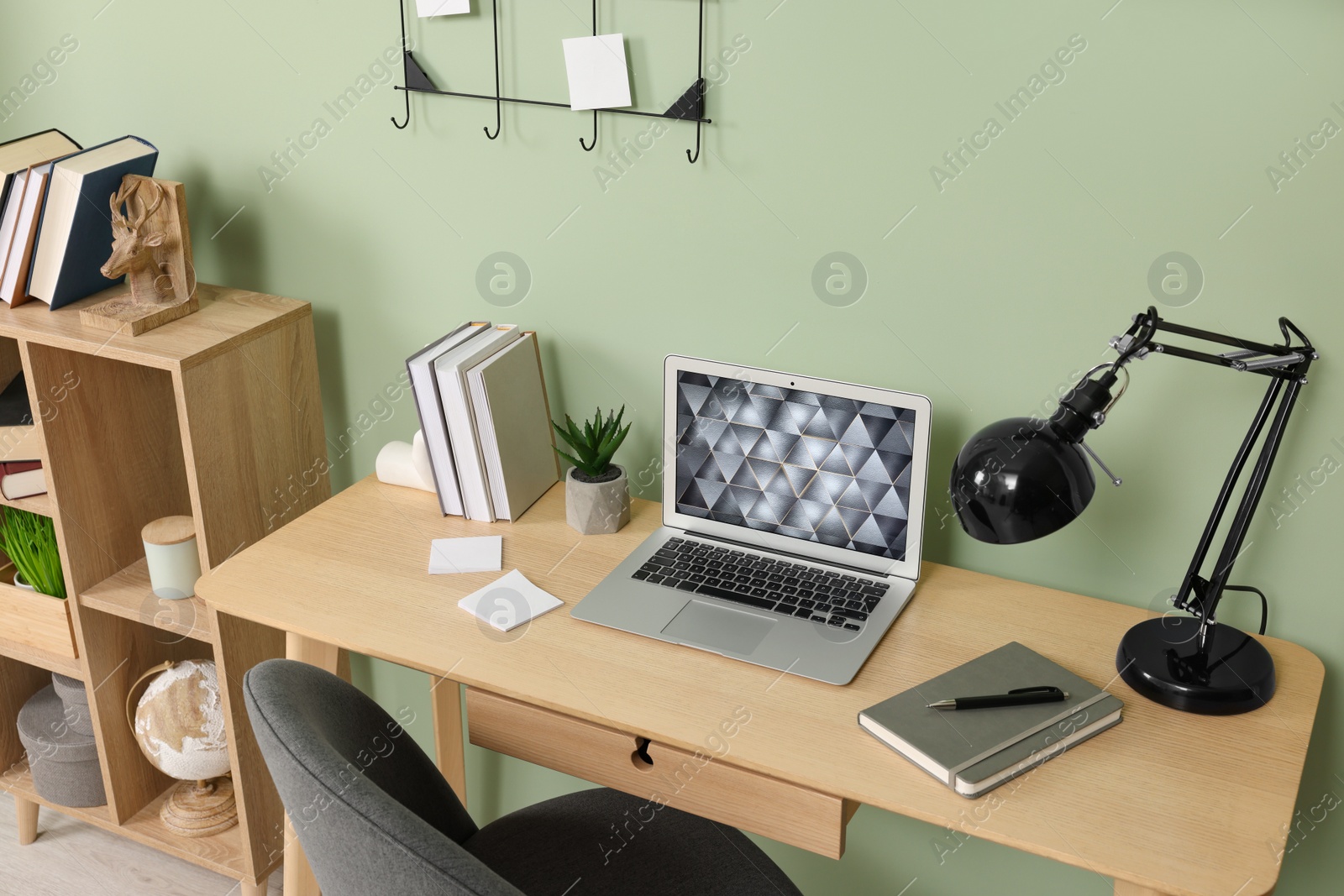 Photo of Modern laptop, books, lamp and stationery on wooden desk near green wall. Home office