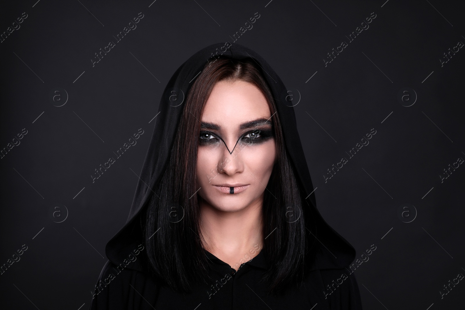 Photo of Mysterious witch in mantle with hood on black background